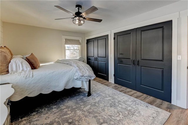 bedroom featuring multiple closets, wood-type flooring, and ceiling fan