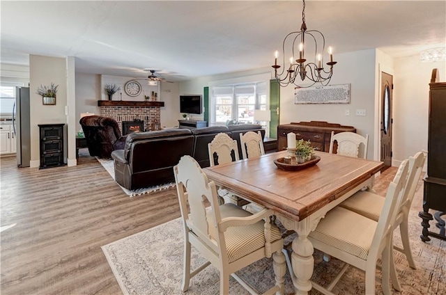 dining room with ceiling fan with notable chandelier, a brick fireplace, and light hardwood / wood-style flooring