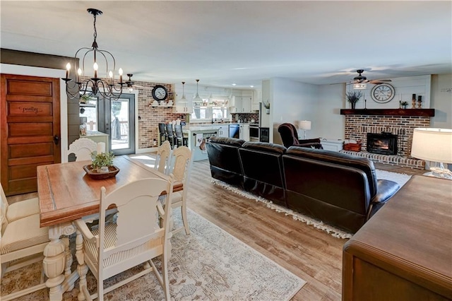 dining room with a brick fireplace, ceiling fan with notable chandelier, and light hardwood / wood-style floors