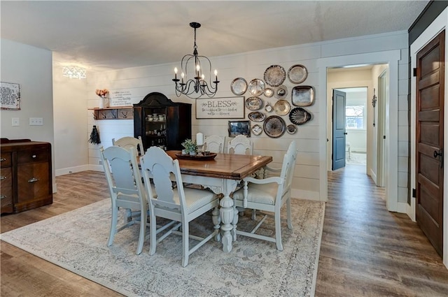 dining area featuring an inviting chandelier, wood-type flooring, and wood walls