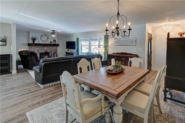 dining room featuring ceiling fan with notable chandelier, a brick fireplace, and light wood-type flooring