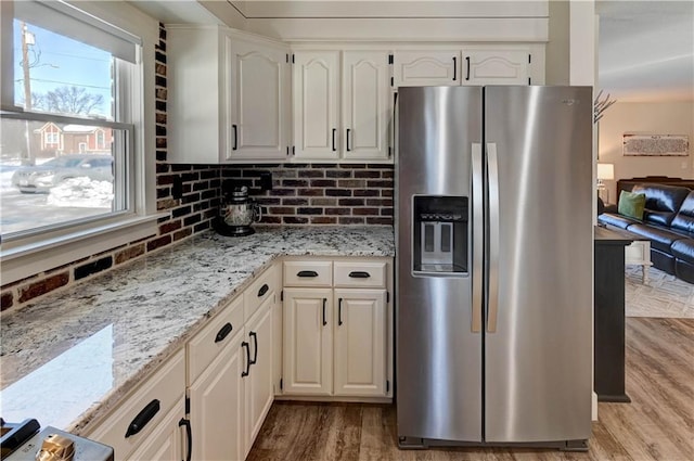 kitchen featuring tasteful backsplash, white cabinetry, light stone counters, stainless steel refrigerator with ice dispenser, and light hardwood / wood-style flooring