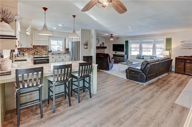 kitchen with a breakfast bar area, appliances with stainless steel finishes, white cabinetry, a healthy amount of sunlight, and decorative light fixtures