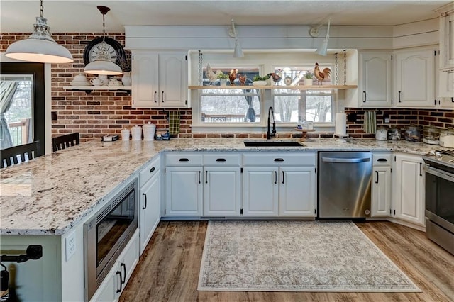 kitchen featuring sink, light hardwood / wood-style flooring, appliances with stainless steel finishes, white cabinetry, and brick wall