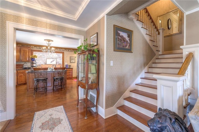 stairway with a notable chandelier, crown molding, and wood-type flooring