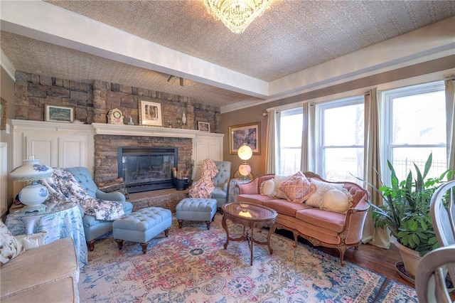 living room featuring hardwood / wood-style flooring, a stone fireplace, a chandelier, and beamed ceiling