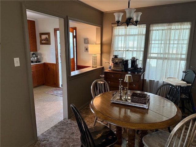 dining space featuring crown molding, light colored carpet, wooden walls, and a notable chandelier