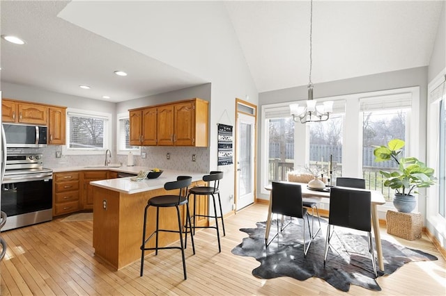 kitchen with sink, hanging light fixtures, light wood-type flooring, kitchen peninsula, and stainless steel appliances