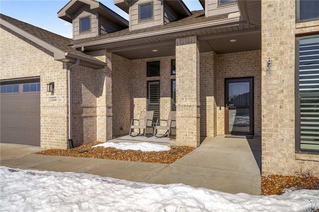 snow covered property entrance with a garage and covered porch