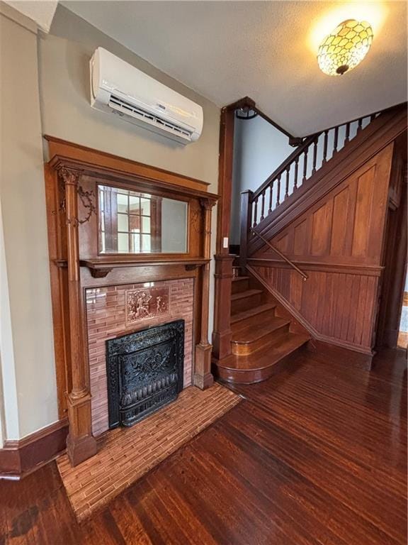 unfurnished living room with an AC wall unit, dark wood-type flooring, and a tiled fireplace