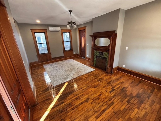 unfurnished living room with an AC wall unit, dark wood-type flooring, a chandelier, and a tiled fireplace