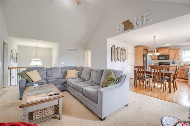 living room with high vaulted ceiling, light wood-type flooring, and a chandelier