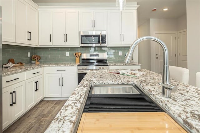 kitchen with backsplash, white cabinetry, dark wood-type flooring, light stone countertops, and stainless steel appliances