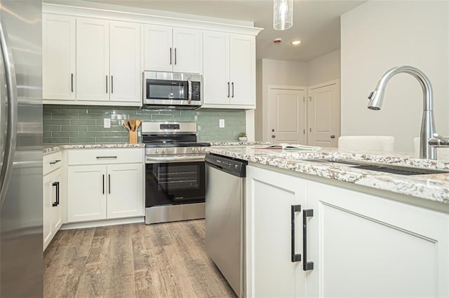 kitchen with light stone countertops, white cabinets, stainless steel appliances, sink, and light hardwood / wood-style flooring