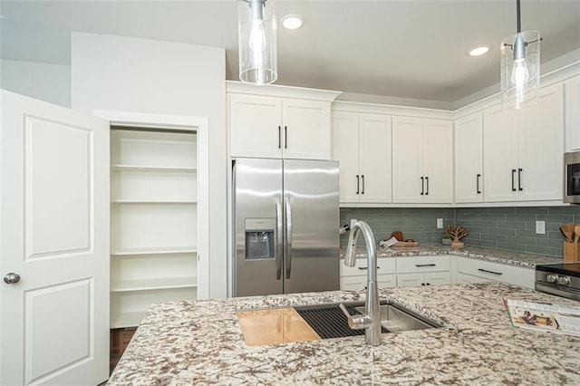 kitchen with decorative backsplash, white cabinets, hanging light fixtures, and appliances with stainless steel finishes