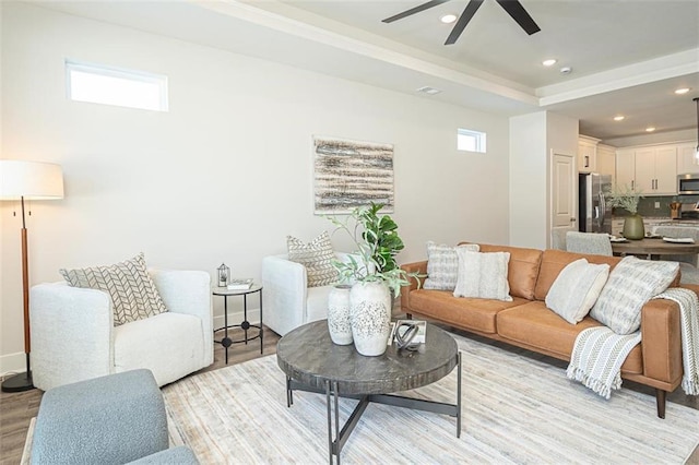 living room featuring light wood-type flooring, ceiling fan, and a tray ceiling