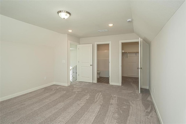 unfurnished bedroom featuring a spacious closet, lofted ceiling, a closet, light colored carpet, and ensuite bathroom