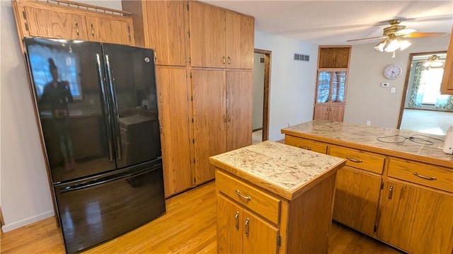 kitchen featuring light hardwood / wood-style floors, black fridge, ceiling fan, and a kitchen island