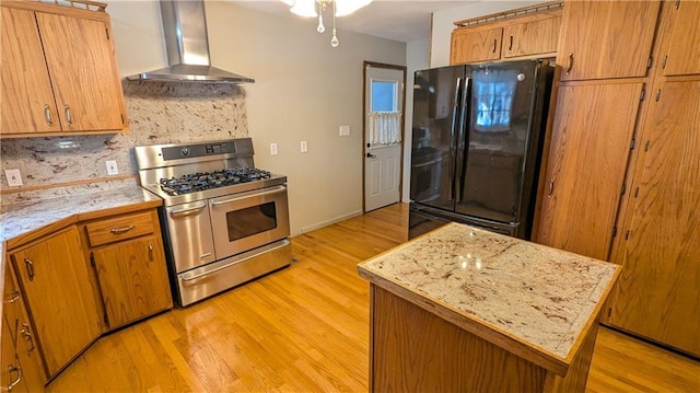 kitchen with wall chimney exhaust hood, range with two ovens, backsplash, black fridge, and light wood-type flooring