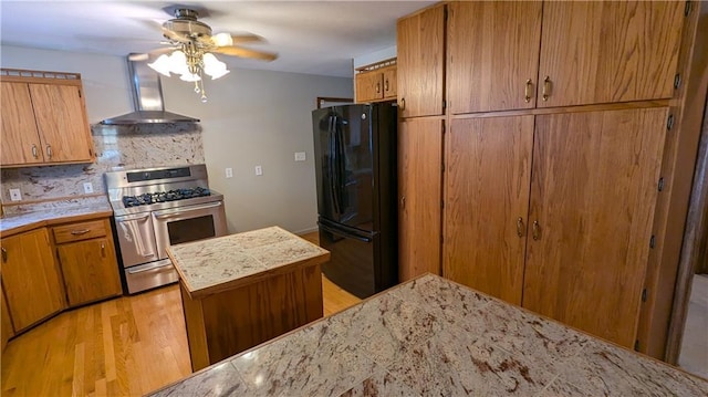 kitchen with light hardwood / wood-style floors, wall chimney range hood, black fridge, backsplash, and range with two ovens