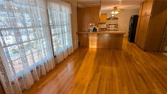 kitchen featuring stainless steel range oven, decorative backsplash, black fridge, kitchen peninsula, and hardwood / wood-style flooring