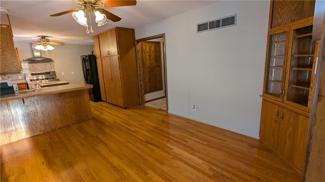 kitchen with kitchen peninsula, stainless steel range oven, black refrigerator, and light hardwood / wood-style floors