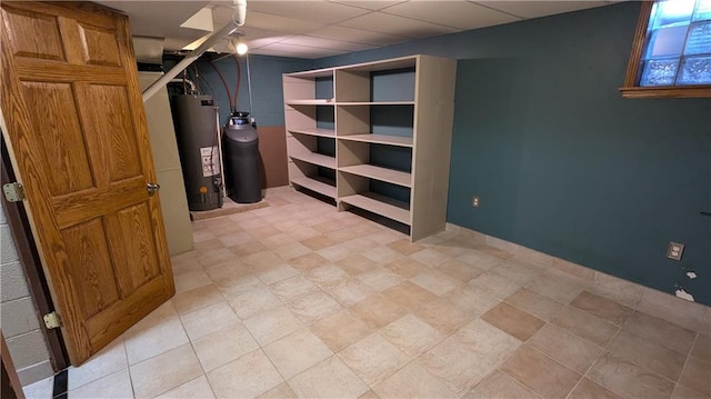 basement with a paneled ceiling and water heater