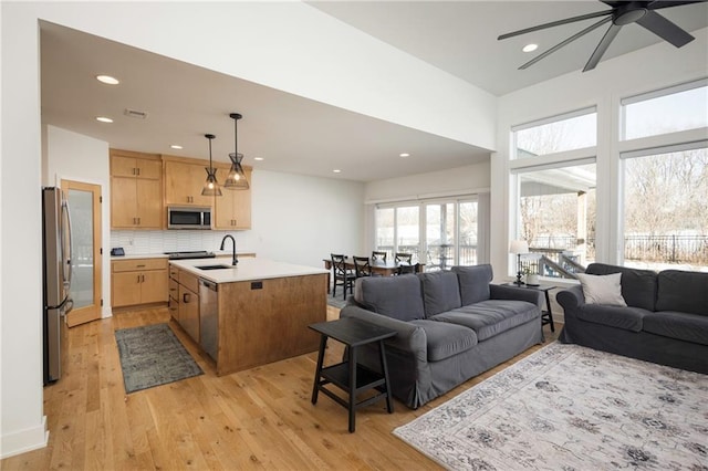 kitchen with light hardwood / wood-style flooring, sink, decorative light fixtures, a center island with sink, and stainless steel appliances