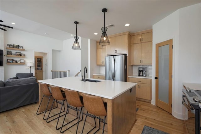 kitchen featuring open floor plan, freestanding refrigerator, light brown cabinetry, light wood-type flooring, and a sink