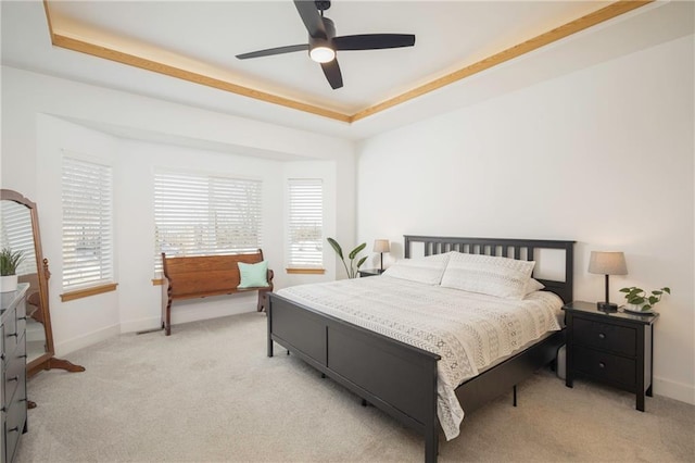 bedroom with light carpet, ceiling fan, a raised ceiling, and baseboards