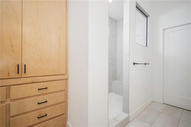 bathroom with tiled shower, baseboards, and tile patterned floors