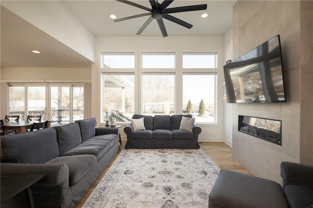 living area featuring light wood finished floors, ceiling fan, a tiled fireplace, and recessed lighting