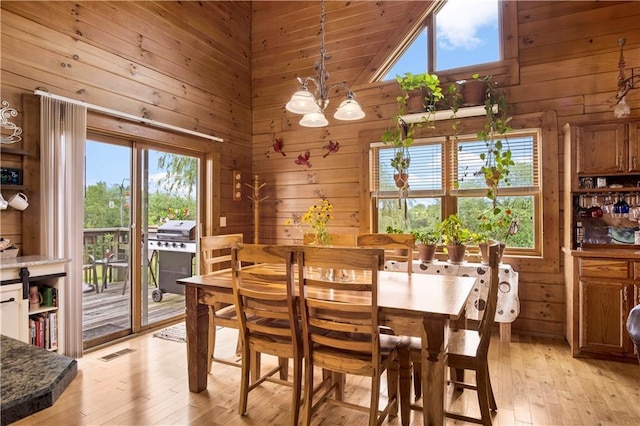 dining space with an inviting chandelier, high vaulted ceiling, light hardwood / wood-style floors, and wood walls