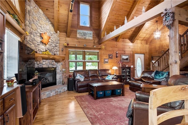 living room featuring beam ceiling, wood walls, wood ceiling, light wood-type flooring, and a fireplace