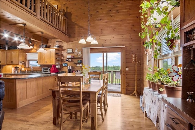 dining space with a towering ceiling, wooden walls, sink, and light hardwood / wood-style flooring