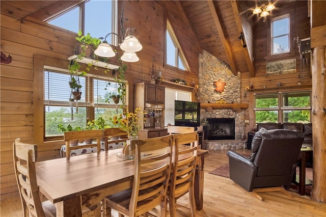 dining room featuring a stone fireplace, wood ceiling, wooden walls, and light hardwood / wood-style flooring