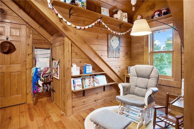 sitting room with lofted ceiling, light wood-type flooring, and wood walls