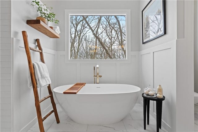 bathroom featuring marble finish floor, a decorative wall, and a freestanding bath