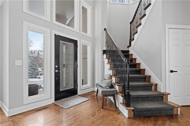 foyer entrance featuring visible vents, a high ceiling, wood finished floors, baseboards, and stairs