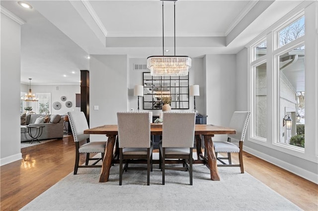 dining room featuring crown molding, wood finished floors, a raised ceiling, and an inviting chandelier