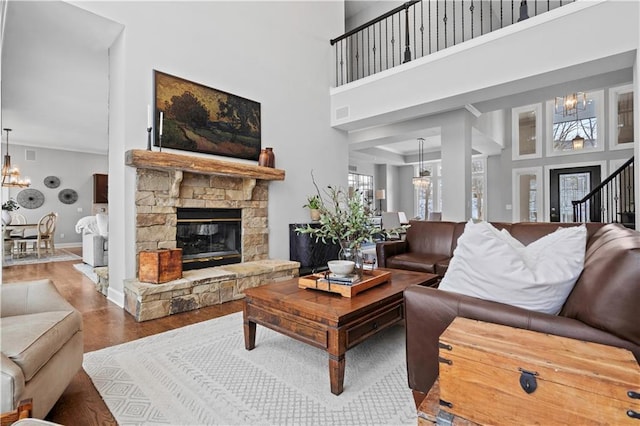 living area featuring an inviting chandelier, baseboards, wood finished floors, and a stone fireplace