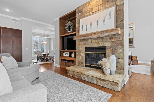 living room featuring crown molding, a fireplace, visible vents, wood finished floors, and baseboards