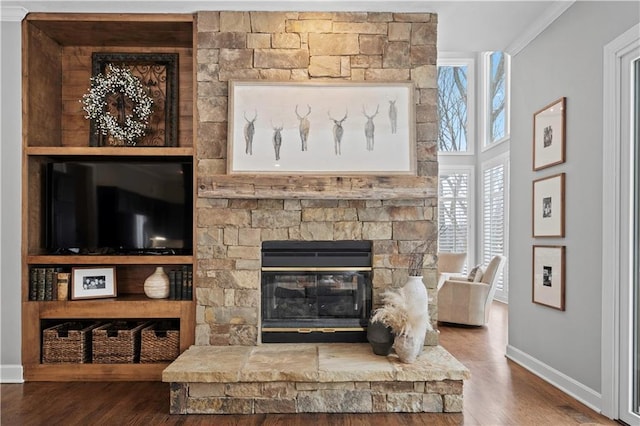 living area featuring crown molding, a stone fireplace, baseboards, and wood finished floors