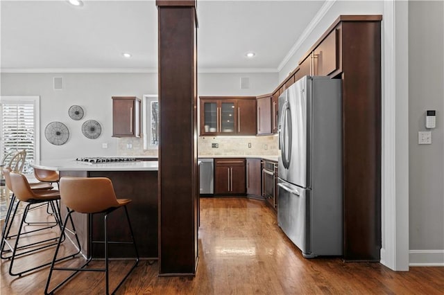 kitchen featuring a breakfast bar, light countertops, appliances with stainless steel finishes, ornamental molding, and wood finished floors