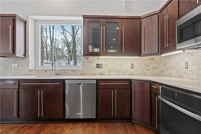 kitchen featuring dark wood-style flooring, stainless steel appliances, light countertops, glass insert cabinets, and a sink