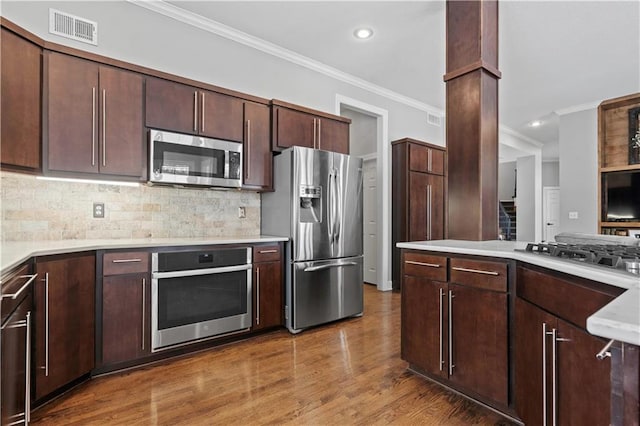 kitchen featuring stainless steel appliances, visible vents, ornamental molding, and wood finished floors