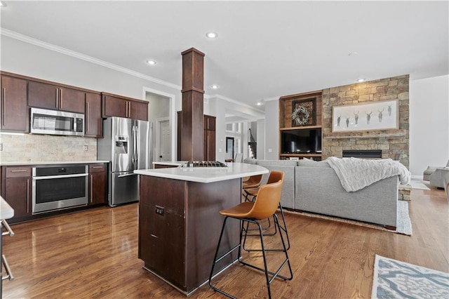 kitchen with a center island, stainless steel appliances, light countertops, dark brown cabinets, and a kitchen bar