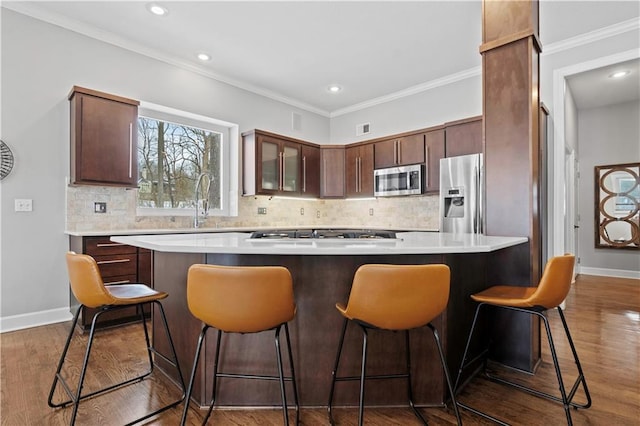 kitchen with a breakfast bar area, dark wood-type flooring, baseboards, ornamental molding, and appliances with stainless steel finishes