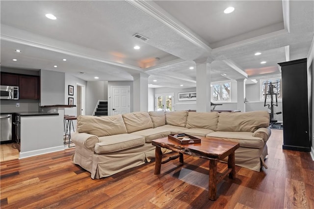 living room featuring light wood-type flooring, decorative columns, visible vents, and stairway