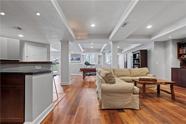 living area featuring crown molding, visible vents, decorative columns, and wood finished floors